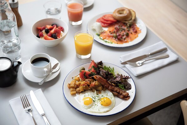 A breakfast table with plates of food, a coffee cup, a glass of orange juice, and a water bottle.