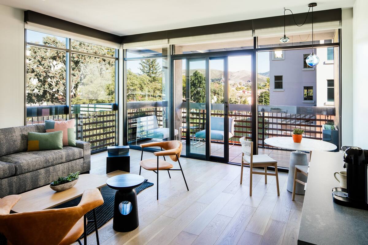 A modern living room with a sofa, chairs, a coffee machine, and a dining area with a table and chairs.