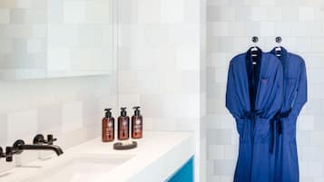 A modern bathroom with a white tiled wall, a large mirror, a white sink, and two blue robes hanging on hooks.