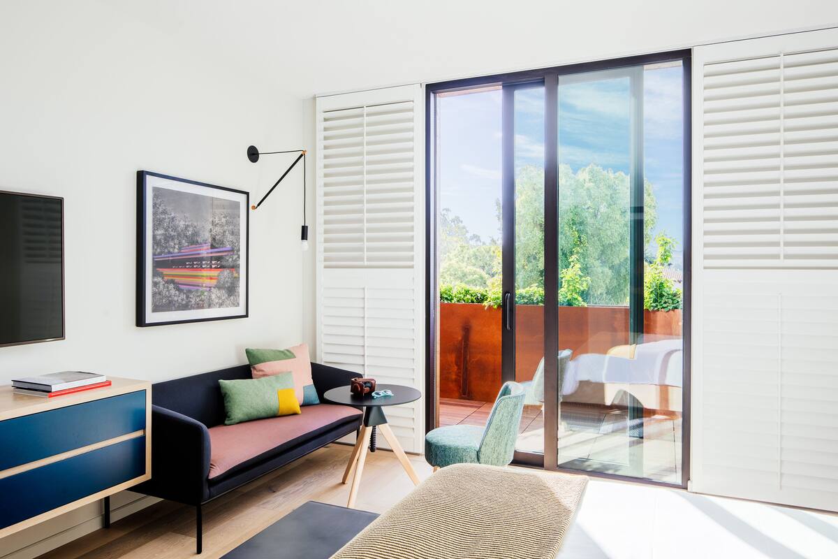 A modern living room with a sofa, a small table, and a TV. There is a sliding glass door leading to an outdoor area with a chair and a table.