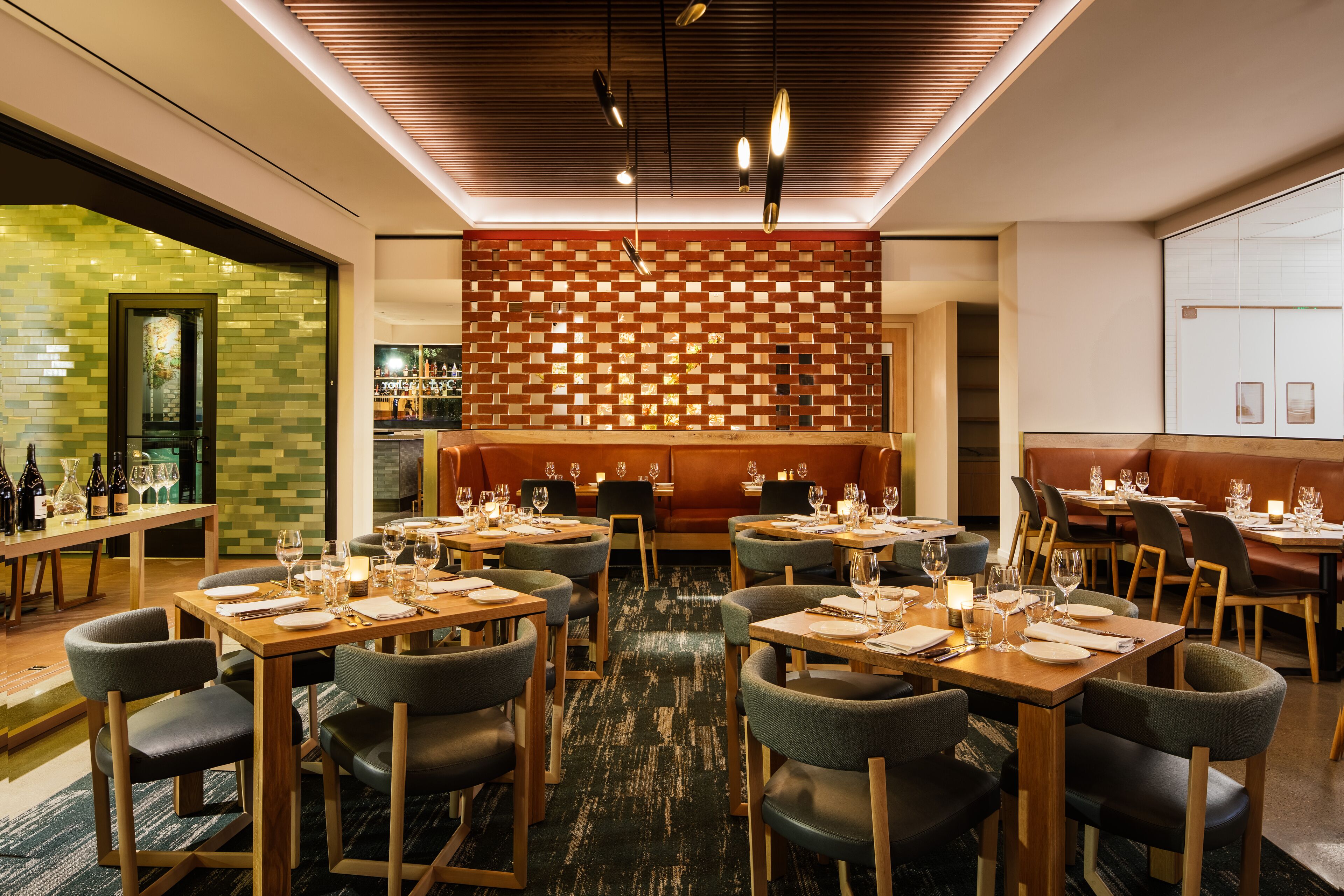 A restaurant with multiple dining tables and chairs, a patterned wall, and a bar area.