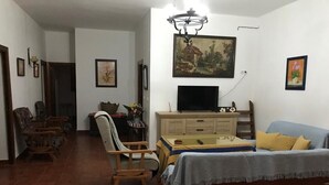 Una sala de estar con sofá, televisor, aparador de madera y zona de comedor con sillas.