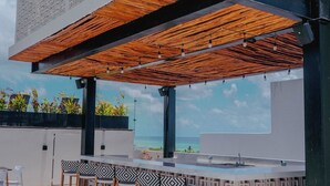 Un bar en la azotea con diseño geométrico, mesas al aire libre y vistas al océano.