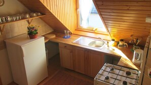 A compact kitchen with a refrigerator, sink, stove, and wooden cabinets.