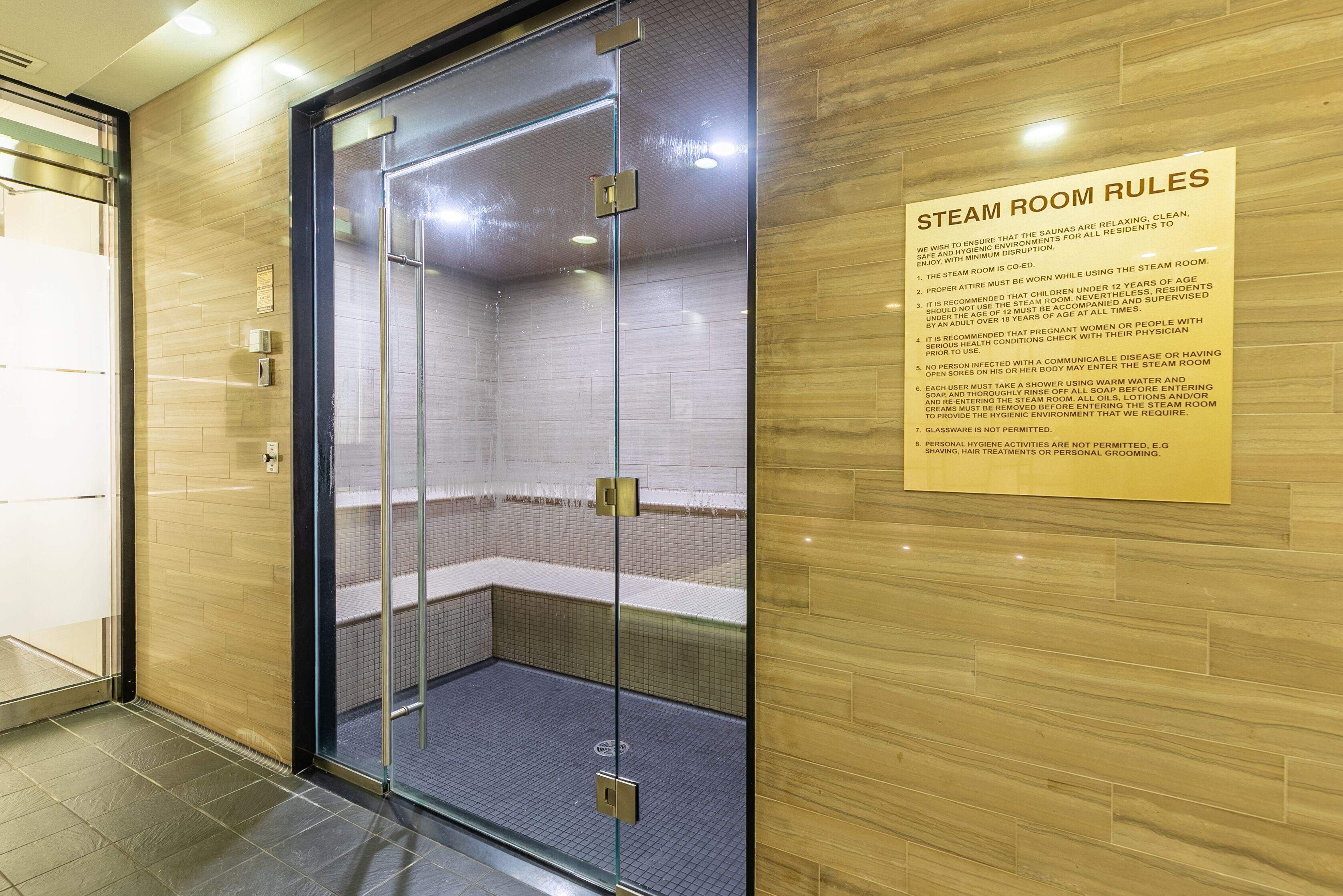 Un hammam avec une porte en verre et un panneau indiquant les règles à respecter.