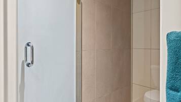 A modern bathroom with a glass shower enclosure, beige tiles, and a striped bath mat.