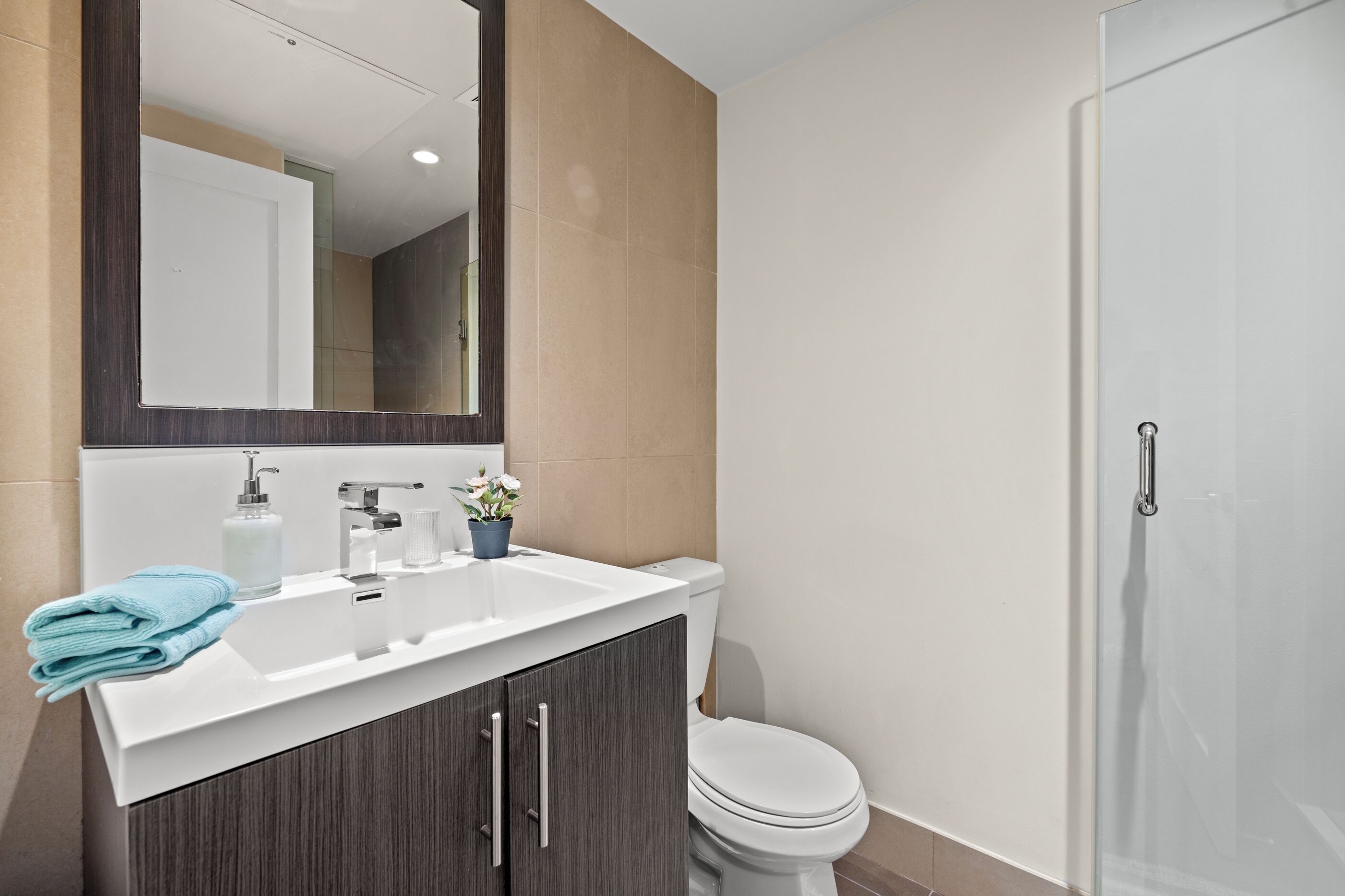 A modern bathroom with a white sink, dark wood cabinets, a glass shower enclosure, and a white toilet.