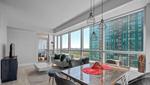 A modern living room with a glass dining table, grey upholstered chairs, and a sofa with green cushions. - Modern Apartments in North York (Toronto)