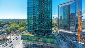 A high-rise building with a glass facade, surrounded by construction cranes and a busy street. - Modern Apartments in North York (Toronto)