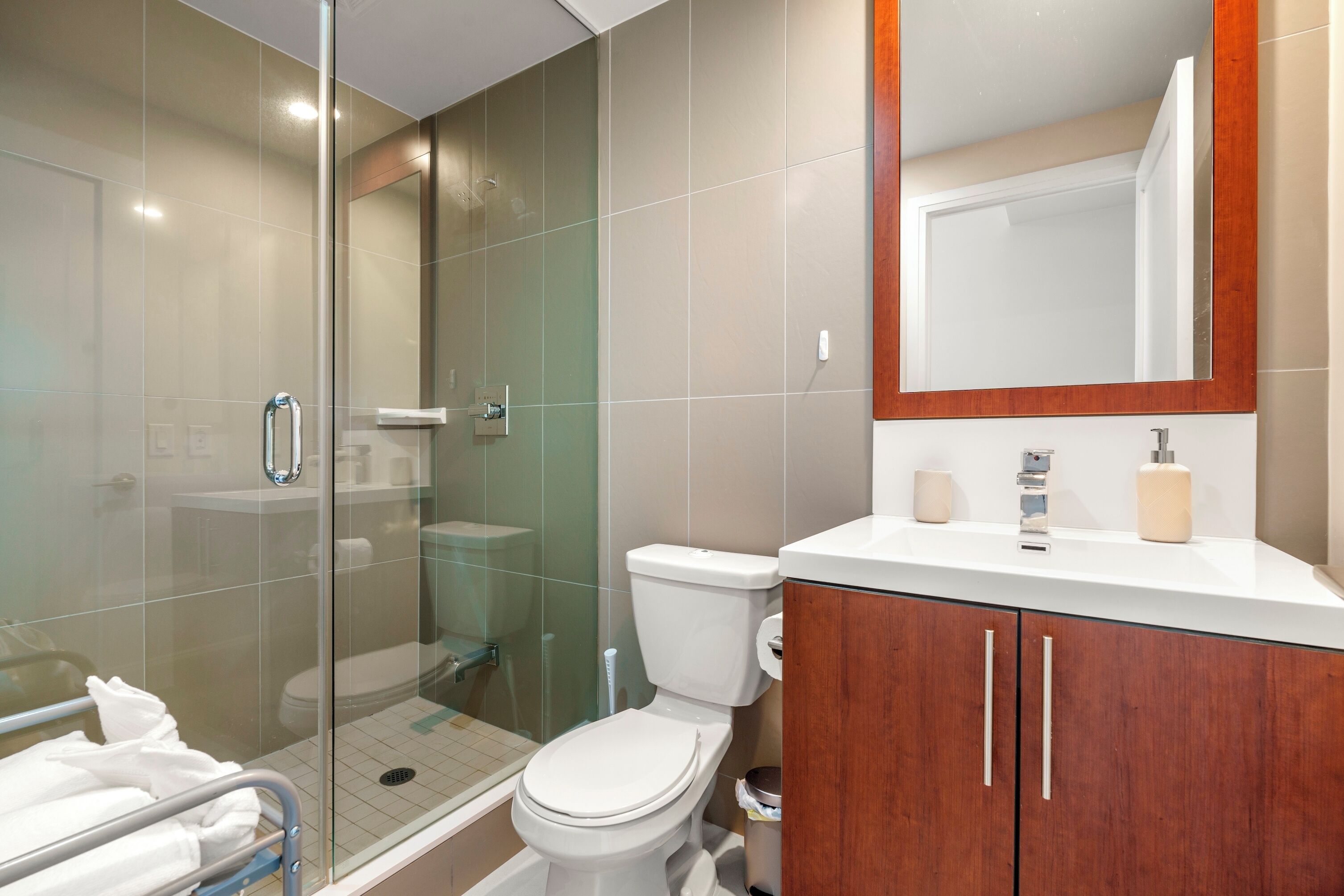 A modern bathroom with a glass-enclosed shower, a white toilet, and a wooden vanity with a mirror.