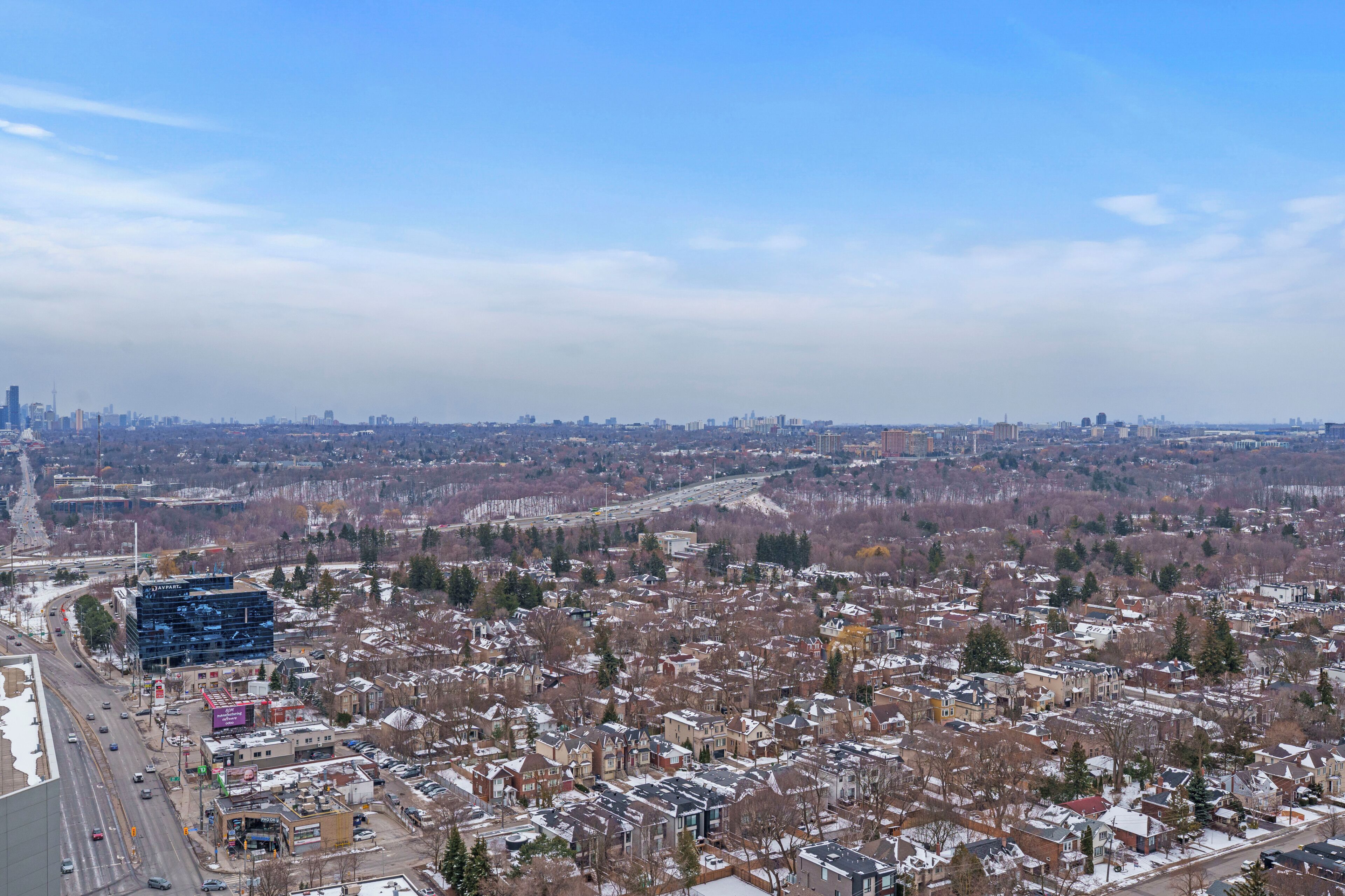 Une vue urbaine mêlant bâtiments résidentiels et commerciaux, un ciel dégagé et une autoroute au premier plan.