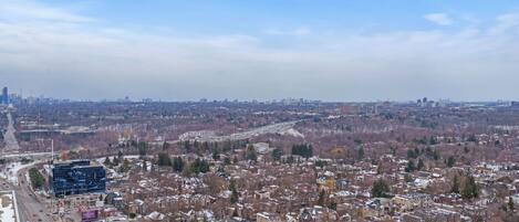 Une vue urbaine mêlant bâtiments résidentiels et commerciaux, un ciel dégagé et une autoroute au premier plan.