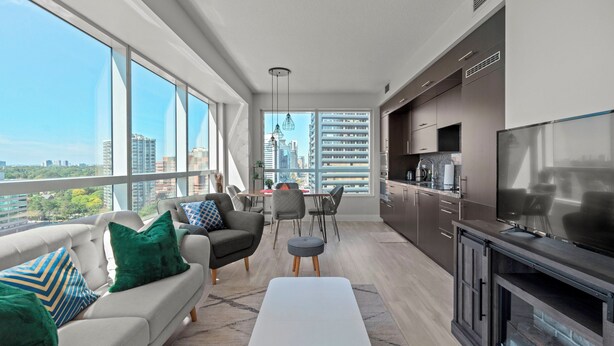 A modern apartment with a balcony, a dining area, a living room with a sofa and ottoman, and a kitchen with a TV and fireplace. - Modern Apartments in North York (Toronto)
