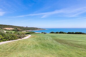 Un parcours de golf offrant une vue dégagée sur l’océan et un phare visible au loin.