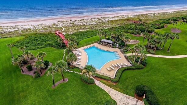 An aerial view of a resort with a swimming pool, palm trees, and a beach. - Amelia Retreat C 3 - Hosted by Moore AI Rentals (Fernandina Beach)