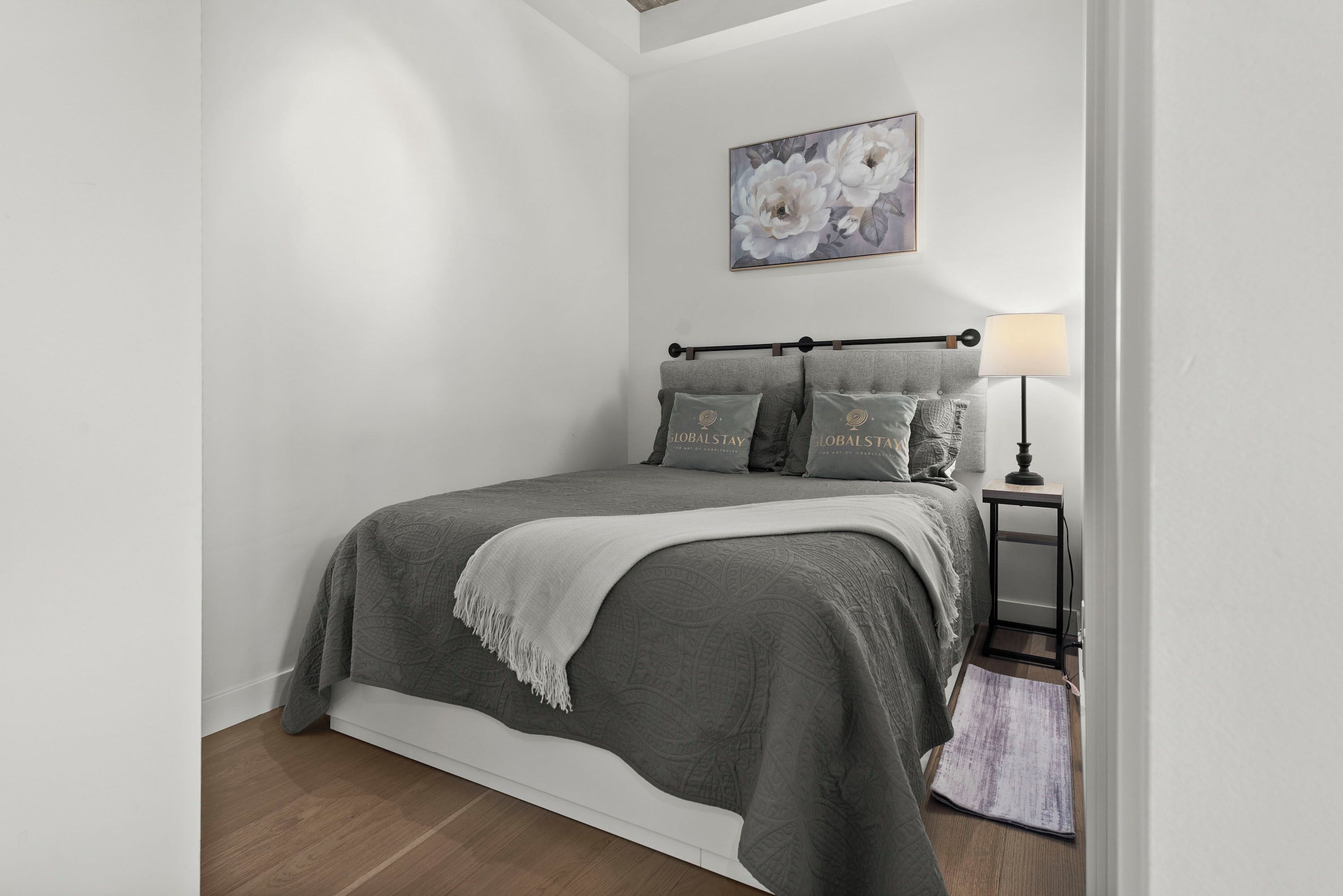 A bedroom with a bed, a nightstand, a lamp, and a floral artwork on the wall.