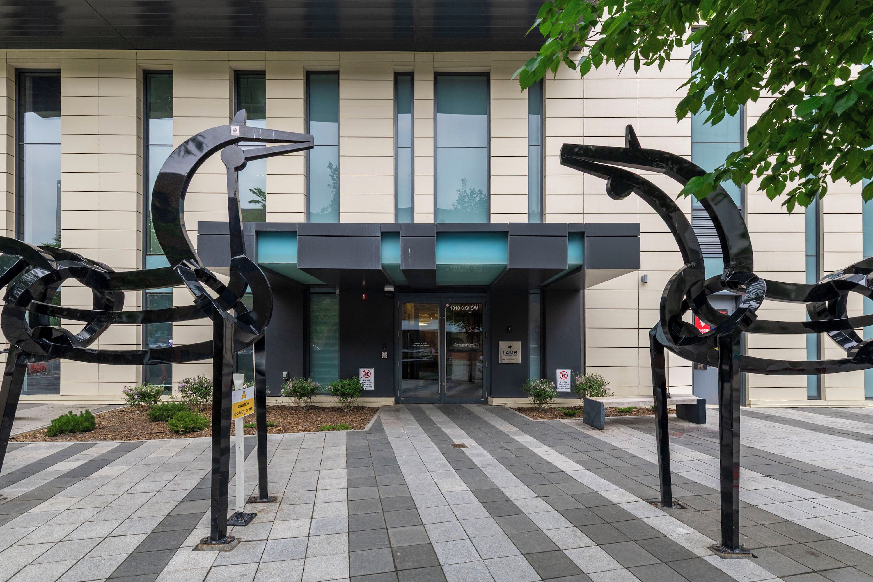 Um edifício moderno com entrada de vidro, rodeado por uma escultura metálica geométrica.