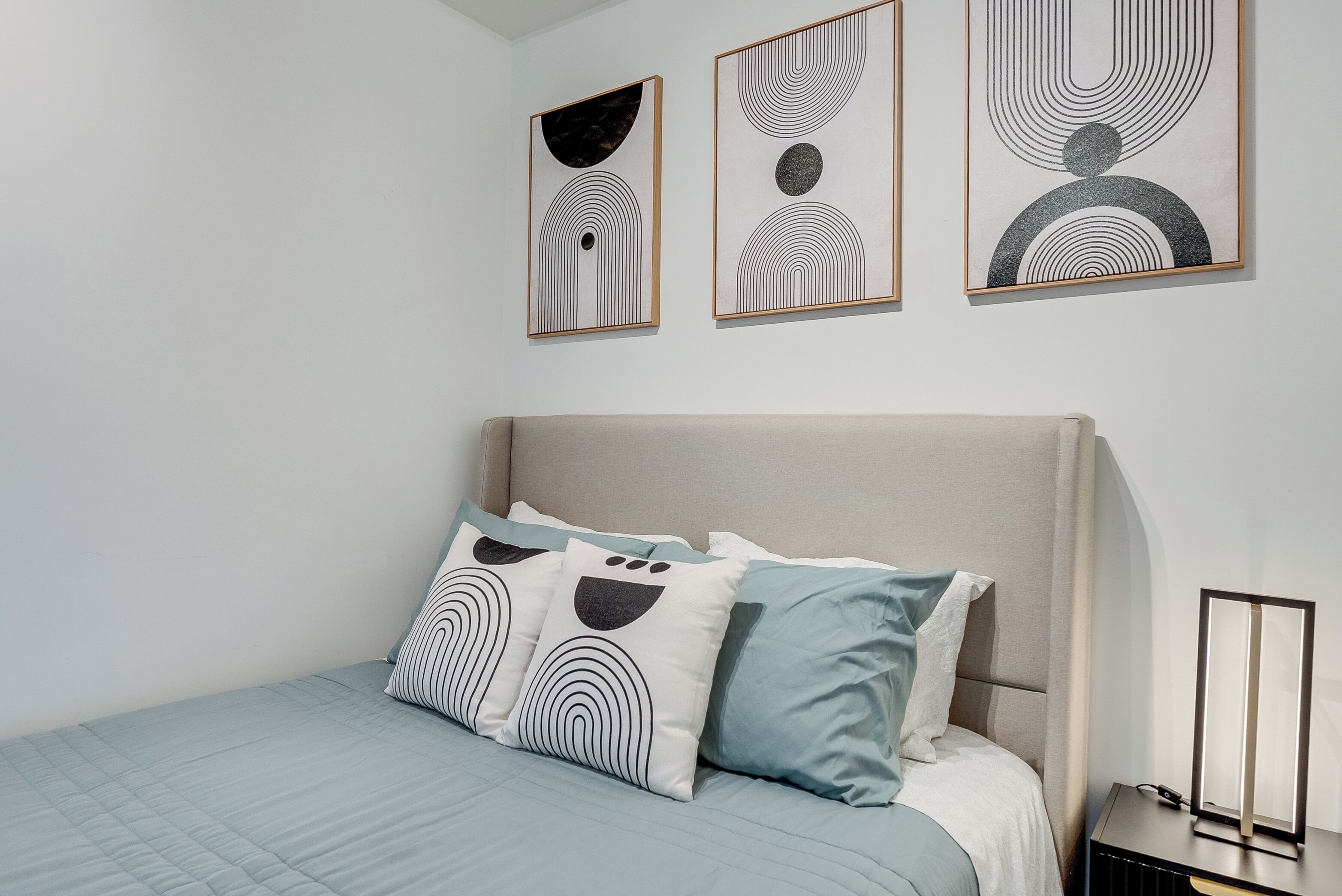A bedroom with a bed, pillows, and three framed artworks on the wall.