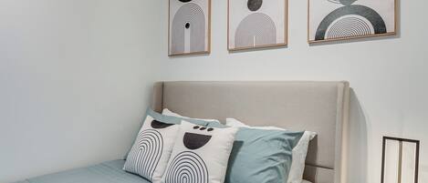 A bedroom with a bed, pillows, and three framed artworks on the wall.