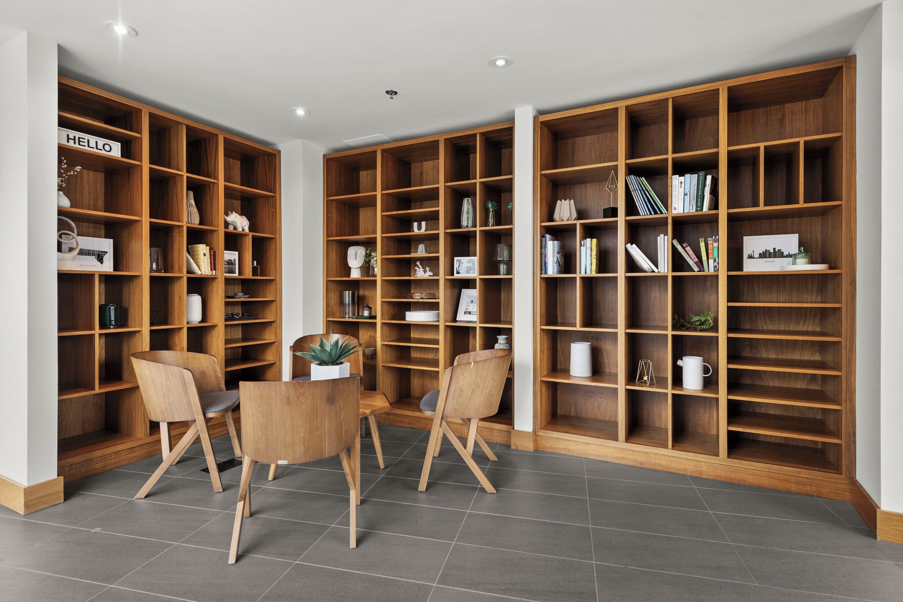 A spacious room with a large wooden bookshelf filled with books and decorative items, a round wooden table with chairs, and a tiled floor.