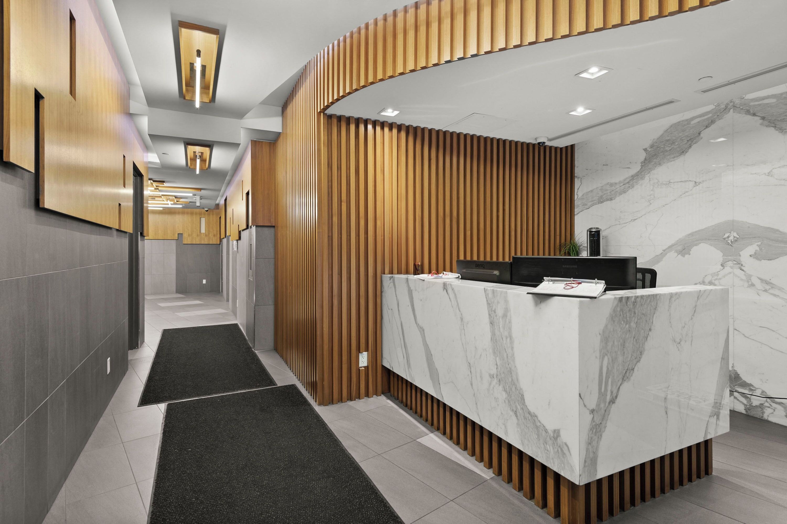 A modern reception area with a marble counter, wooden paneling, and a tiled floor.