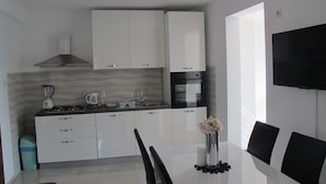 A modern kitchen with white cabinets, a gas stove, a coffee maker, and a sink. There is a dining table with chairs and a vase with flowers. - Comfortable 2 Bedroom Apartment (Mljet)
