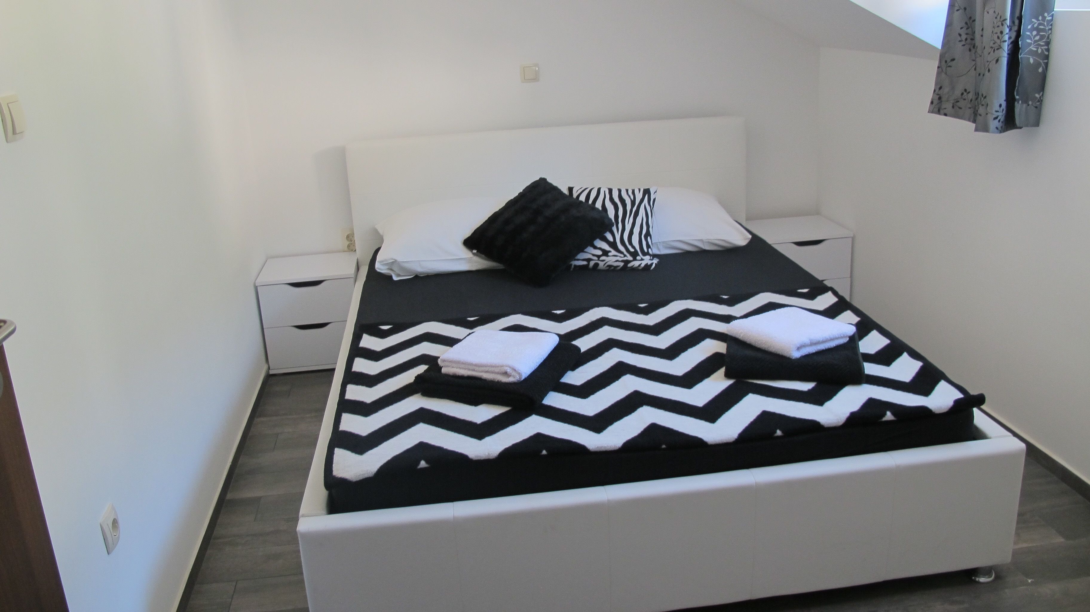 Une petite chambre à coucher, bien rangée, avec un lit, deux tables de chevet et une petite table d’appoint.