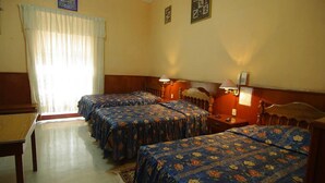 A hotel room with three beds, a wooden headboard, a desk, and a small table. - Hotel Santa Rosa (Ayacucho)