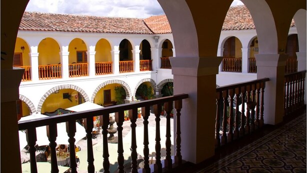 A courtyard with white arches and orange railings, leading to a building with a tiled roof. - Hotel Santa Rosa (Ayacucho)