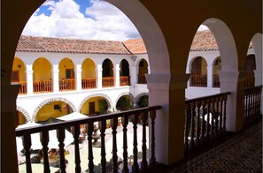 A courtyard with white arches and orange railings, leading to a building with a tiled roof.