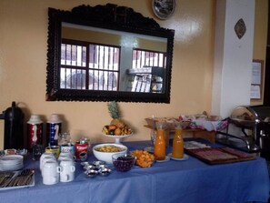 A breakfast buffet setup with various food items, beverages, and utensils on a table.