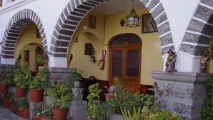 A building with arched entrances, a wooden door, and potted plants. - Hotel Santa Rosa (Ayacucho)