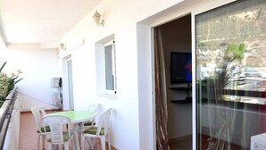 Ein Balkon mit Tisch und Stühlen, eine Schiebeglastür sowie ein Fernseher.