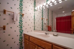 A bathroom with a wooden vanity, a white sink, a mirror with lights, and a red shower curtain. - Golden Bear Inn (Davis)