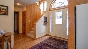 A spacious hallway with wooden flooring, a staircase, a rug, and a door with a ski lift sign. - Golden Bear Inn (Davis)