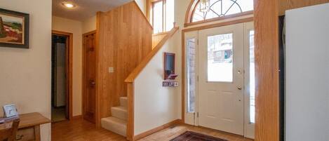 Un hall d’entrée spacieux avec un plancher en bois, un escalier, un tapis et une porte ornée d’un panneau indiquant un télésiège.