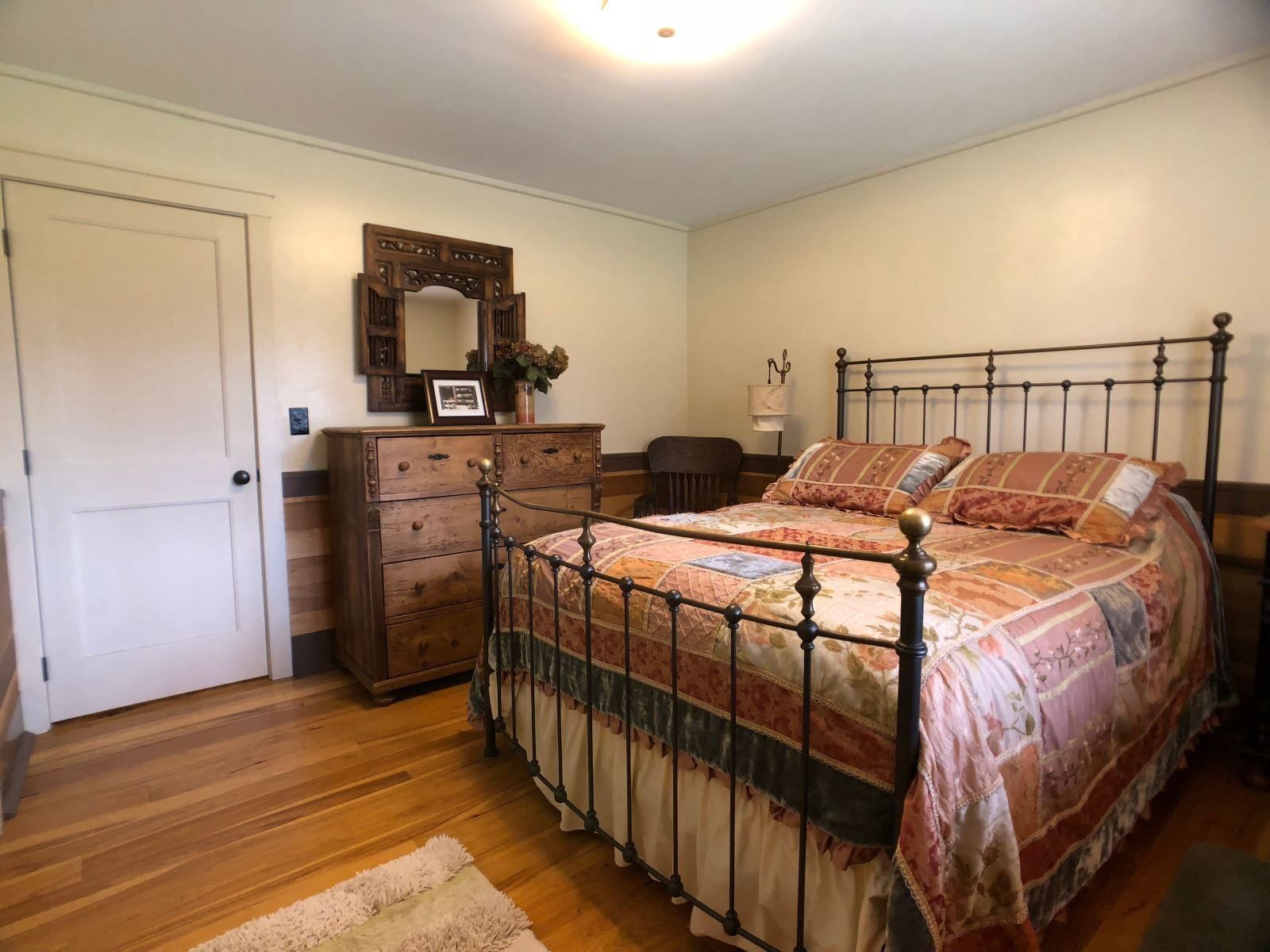 Une chambre à coucher avec un lit en métal, une commode en bois, un miroir et une porte.