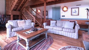 A spacious living room with two striped couches, a wooden coffee table, and a staircase. - Hemlock Lodge (Davis)