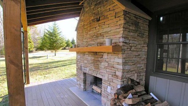 A stone fireplace with a wooden mantel, a wooden deck, and a stack of firewood. - Hemlock Lodge (Davis)