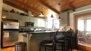 A kitchen with a central island, bar stools, a refrigerator, a microwave, and wooden ceiling beams. - Hemlock Lodge (Davis)