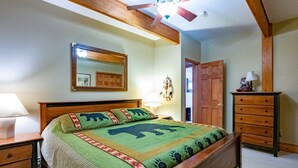 A bedroom with a wooden bed, a nightstand, a dresser, a mirror, and a ceiling fan.