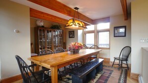 A dining area with a wooden table, black chairs, a bench, a hanging light fixture, a window with blinds, and a patterned rug.