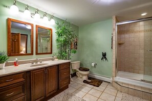 A bathroom with a vanity, two mirrors, a toilet, a shower, and a potted plant.