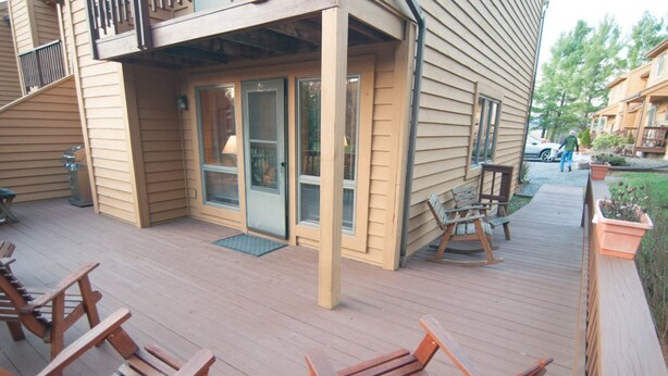A wooden deck with outdoor seating and a glass door entrance.
