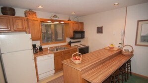 A kitchen with wooden cabinets, a microwave, a stove, and a large wooden island with stools.