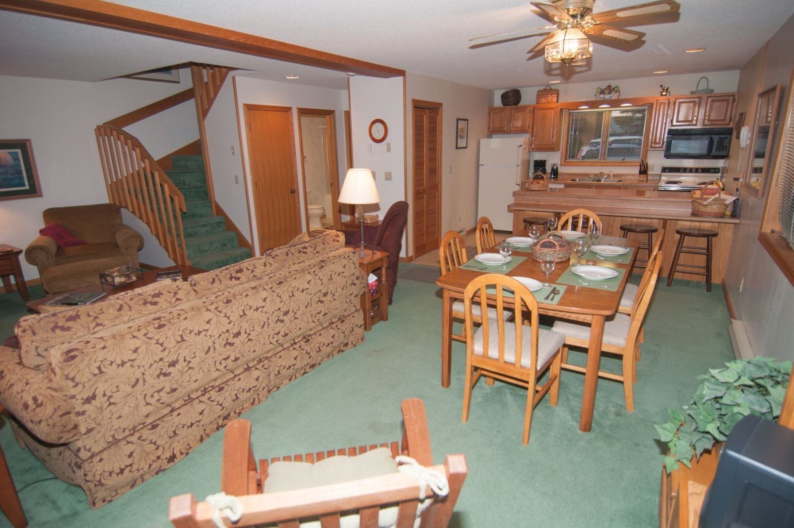A living room with a sofa, dining table, chairs, a staircase, and a kitchen area with appliances.