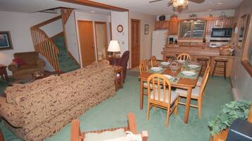 A living room with a sofa, dining table, chairs, a staircase, and a kitchen area with appliances.