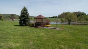 A gazebo in a grassy field with a lake and hills in the background. - Deerfield Village 120 (Davis)