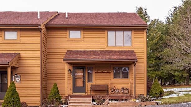 A two-story wooden house with a front porch, a mailbox, and a number sign. - Deerfield Village 120 (Davis)