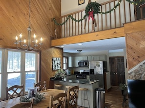 A spacious kitchen with wooden accents, a dining area with a chandelier, and a view of a snowy landscape through large windows. - Gnarnia (Davis)